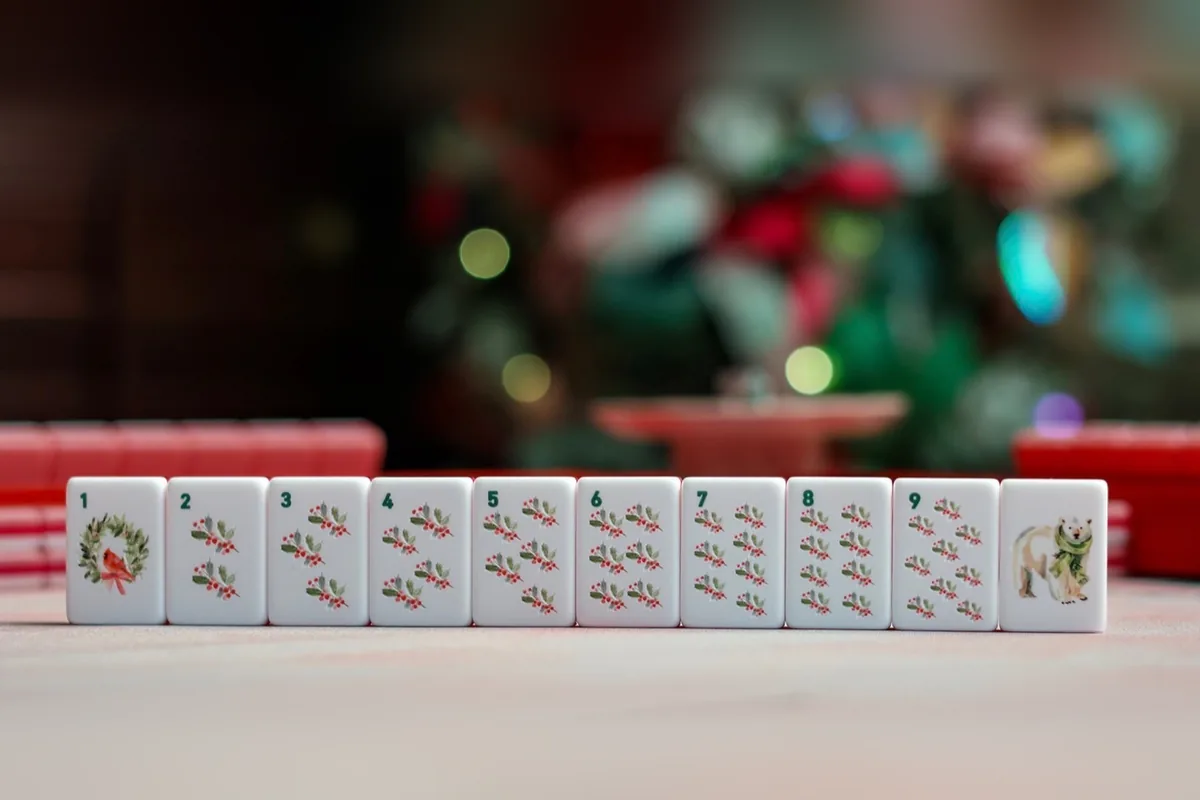 A row of Noel Collection suit tiles numbered 1 to 9 in hand-painted holly sprigs — the 1 a cardinal in a wreath — finished with a polar bear tile, in front of a lit Christmas tree.