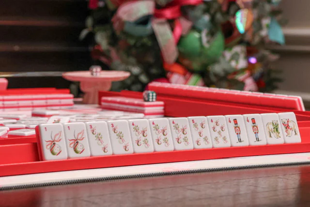A row of Noel Collection tiles on a red rack — ribboned ornaments, holly sprigs, nutcrackers and a polar bear — in front of a decorated Christmas tree.