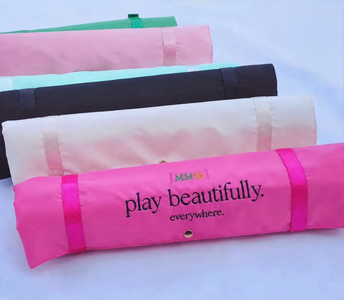 Rolled mmmahjong rack bags — grass green, pink, sky blue, ivory, and hot pink — the hot pink one embroidered &ldquo;play beautifully. everywhere.&rdquo;